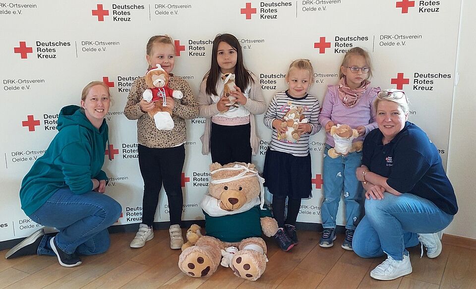 Bild 1: Kinder der  „Langstrümpfe“ – hier vier davon – und des Marienkindergartens waren im Mai und Juni im Rahmen der „Stöbertage“ zu Gast beim DRK-Ortsverein Oelde. Melanie Westerbeck, Vorsitzende des DRK-Ortsvereins (rechts), Lisa Jeßulat, Leiterin  des Jugendrotkreuzes Oelde (links), und Daniela Mitrovic  erklärten den Kindern spielerisch Erste-Hilfe-Maßnahmen an Stofftieren und die vielfältigen Aufgaben der Hilfsorganisation DRK. Foto: DRK Oelde